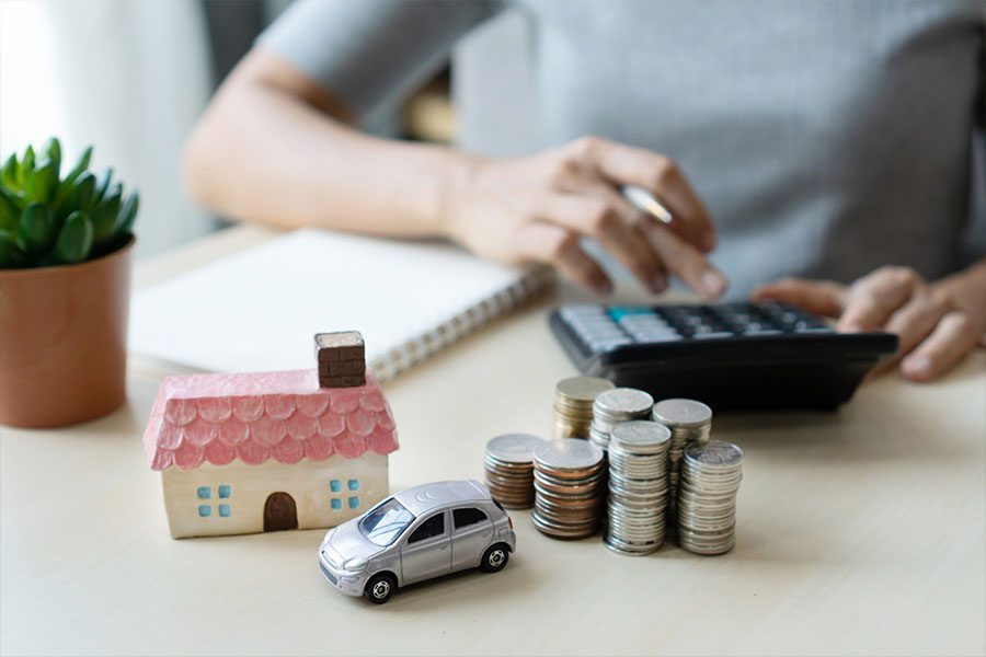 Bundling Home and Auto Insurance - Picture of a Woman's Hands with a House and Car on the Desk