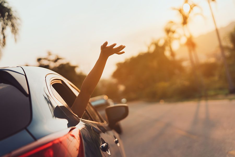 Insurance Quote - View of Woman Sticking Her Hand Out of Car Window at Sunset During Road Trip